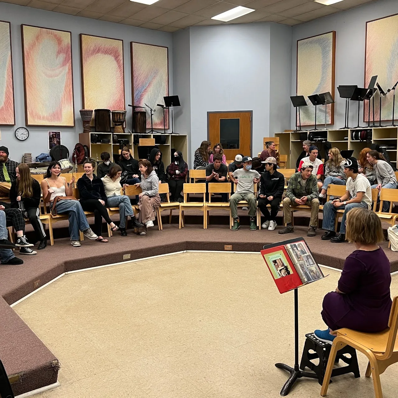 Meg leading a presentation to a large circle of students in a school music room