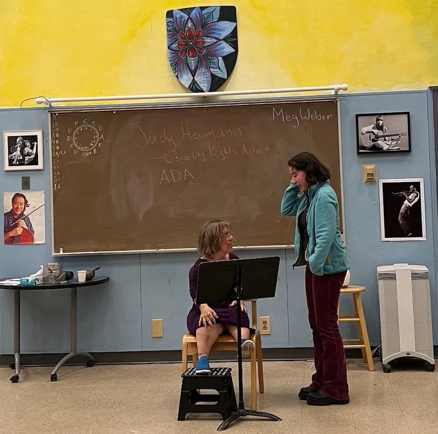 Meg seated and laughing with a student during a classroom visit